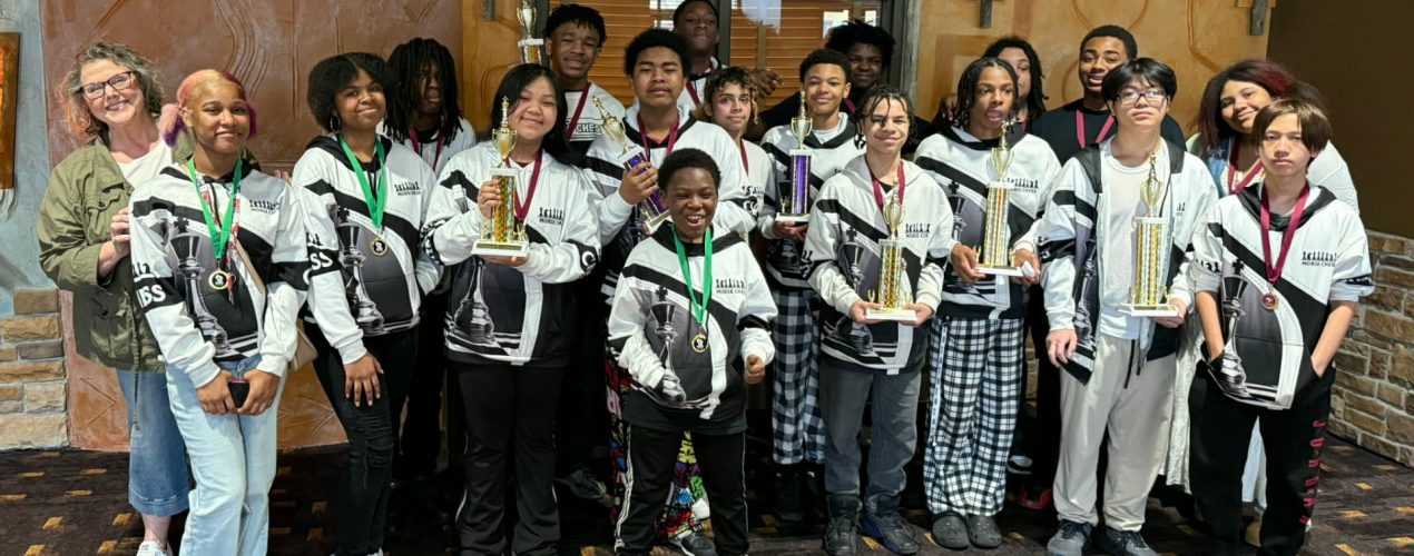 Photo of diverse group of teenagers, all wearing chess sweatshirts and some holding chess trophies