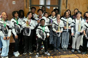 Photo of diverse group of teenagers, all wearing chess sweatshirts and some holding chess trophies